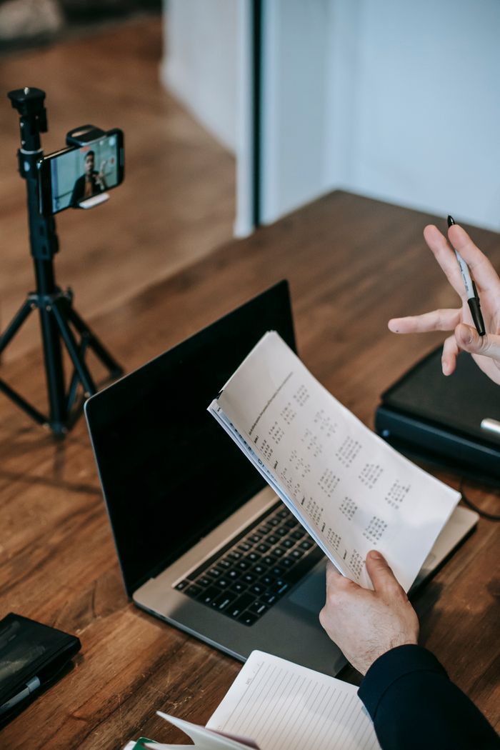 Business professional during a video call, holding documents and gesturing at a laptop workspace.